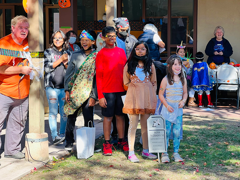 children in halloween costumes wait in line for pinata
