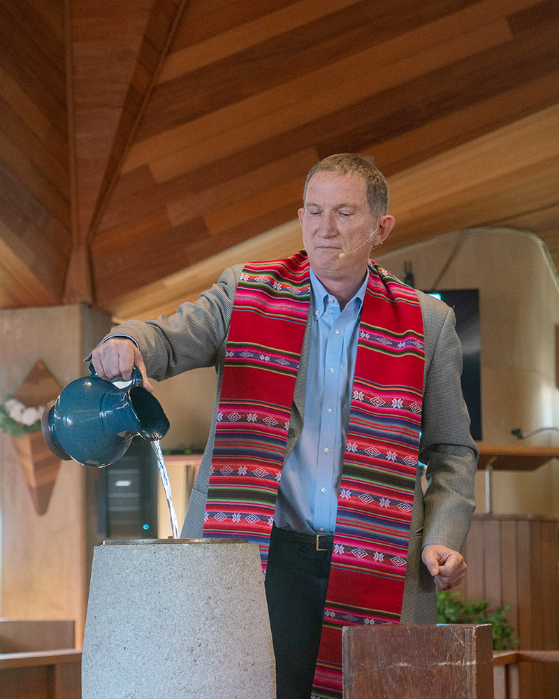 pastor pours holy water from a ceramic pitcher into the baptism bowl