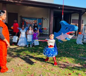 girl in halloween costume swinging at a pinata while other children watch